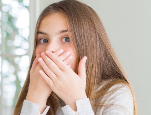 Young girl with something stuck between teeth covering her mouth