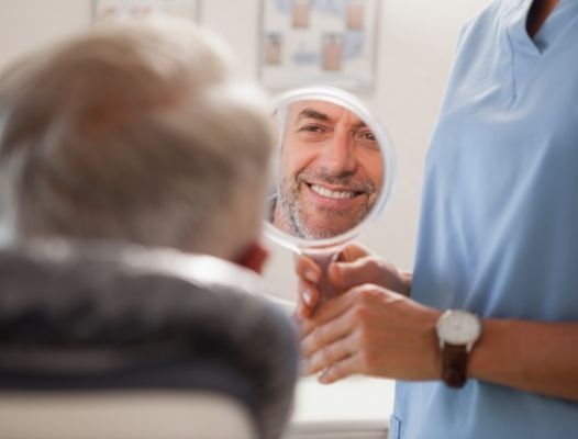 Man looking at smile in mirror after dental implant tooth replacement