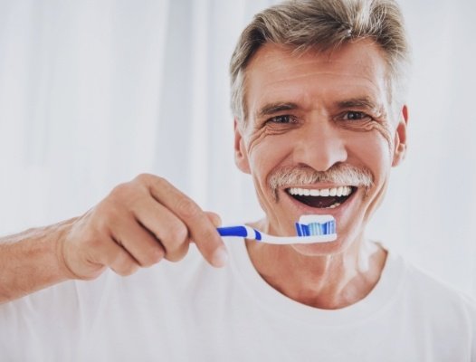 Man brushing teeth to care for smile after dental implant restoration